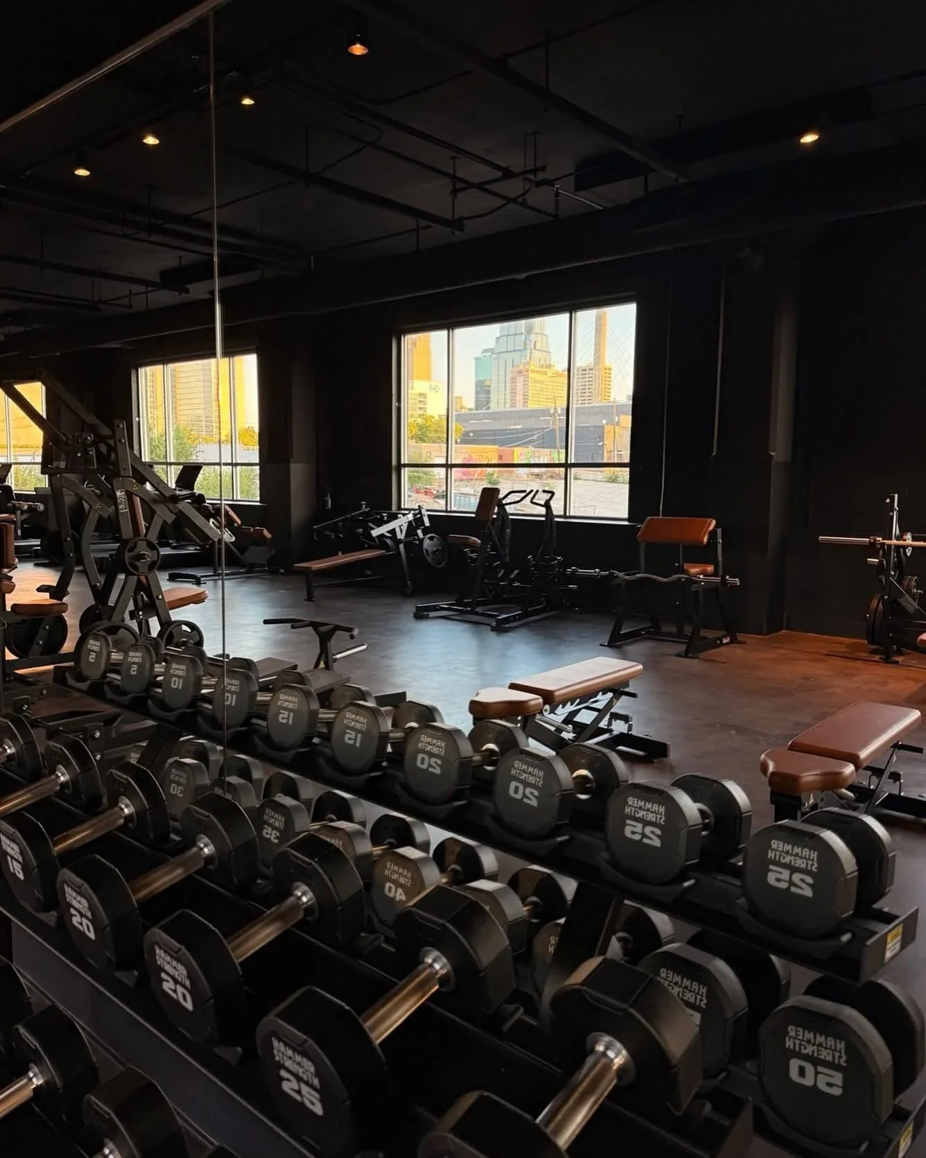 Obsidian’s strength training floor, with black equipment, warm leather benches, and Kansas City skyline views
